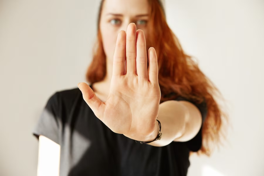 A woman wearing black, her open palm covering her face and facing the camera