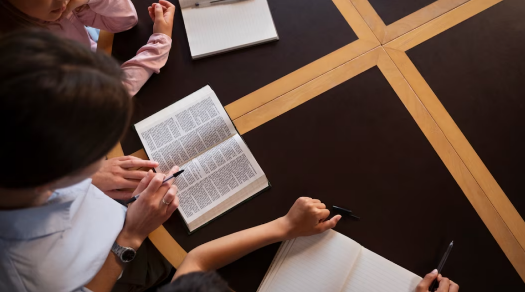 people with pens reading opened books on wooden table