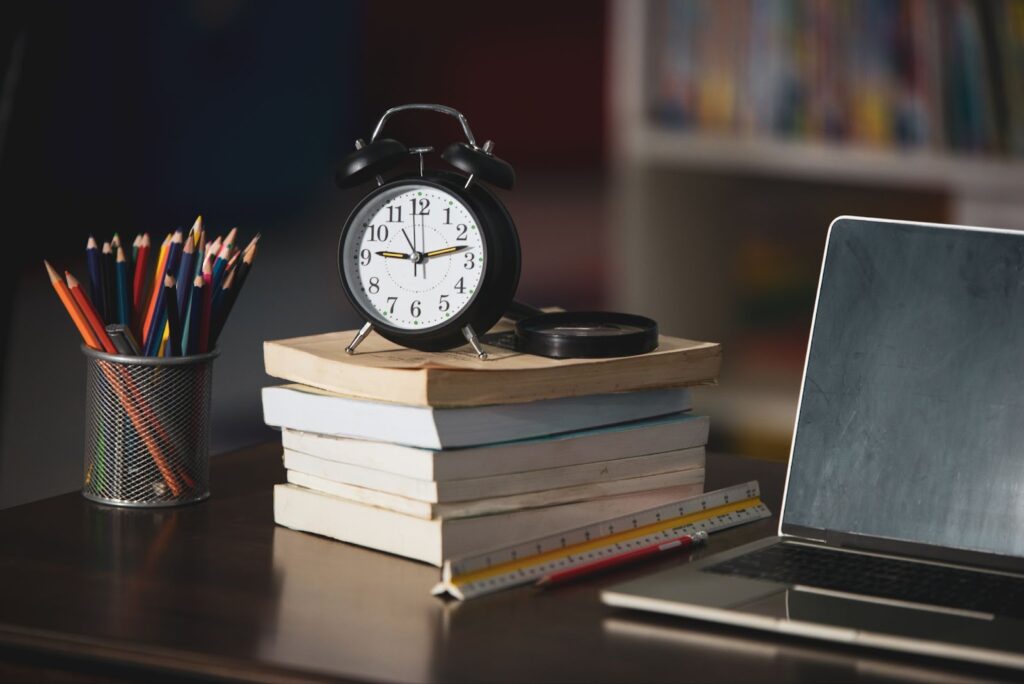 Book, laptop, pencil, clock on wooden table