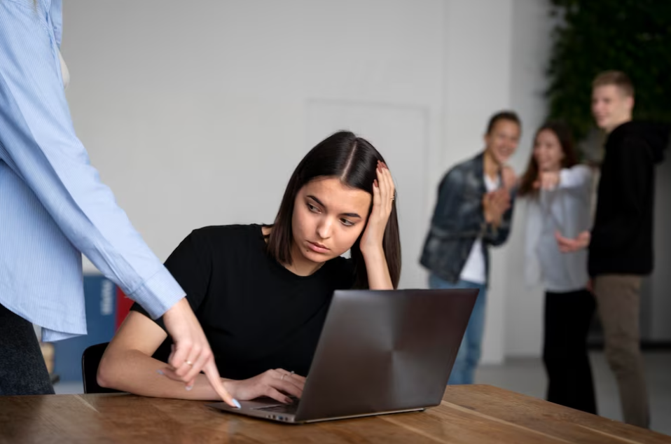 woman in black shirt sitting near the laptop, colleagues smiling at her and pointing with fingers