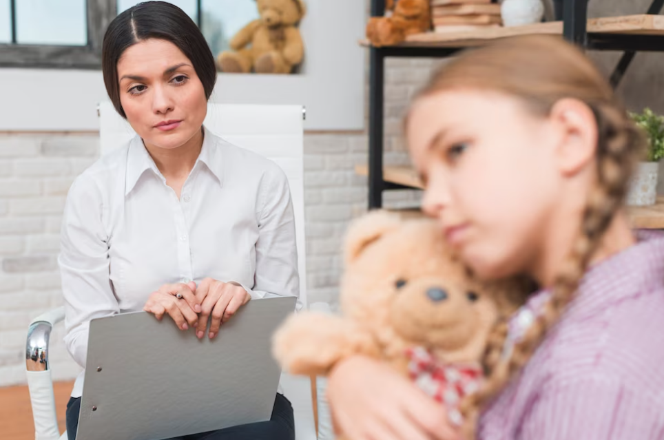 woman sitting in a chair and watching on girl with a teddybear