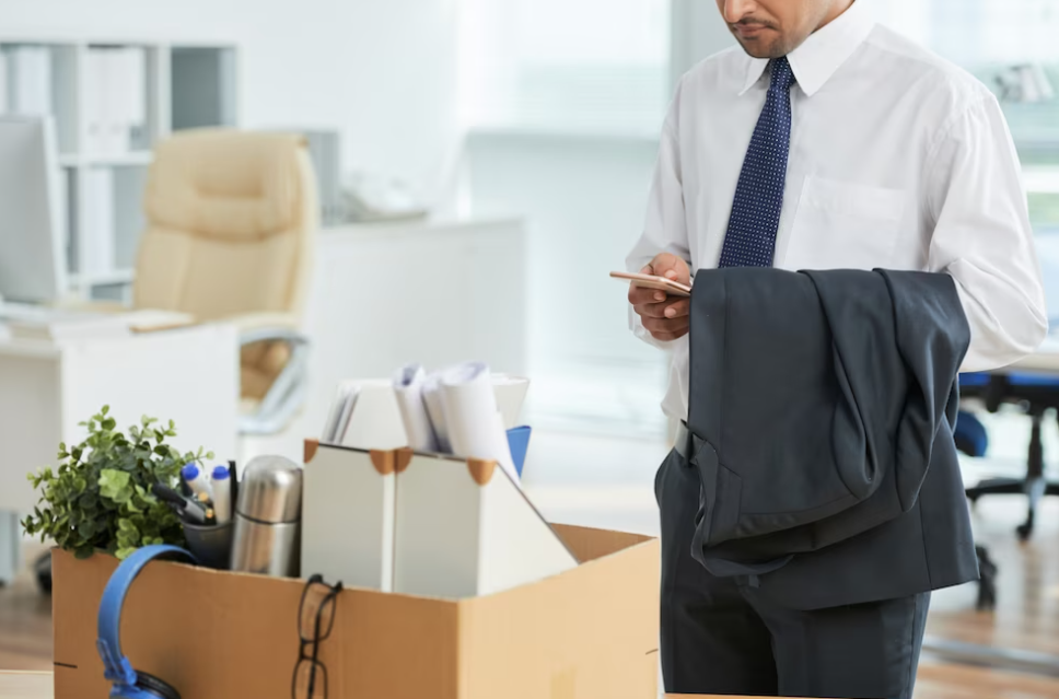 man standing in the office and using a smartphone, with personal belongings in box